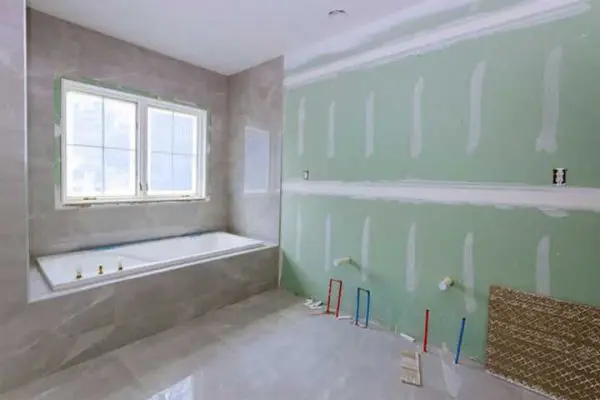 bathroom remodeling project featuring an installed bathtub with gray tile surround next to unfinished green drywall with exposed plumbing lines