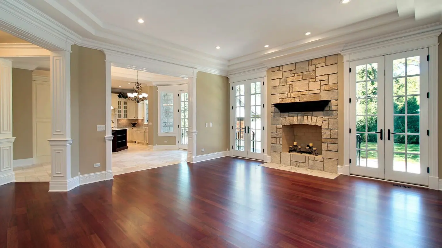 an empty, grand living room showcasing a newly repaired dark hardwood floor, a stone fireplace, a coffered ceiling, and white french doors leading outside