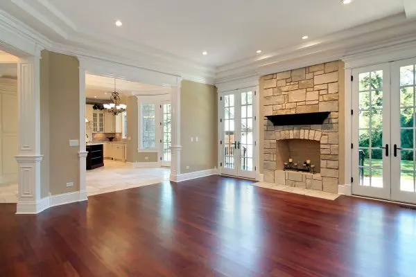 an empty, grand living room showcasing a newly repaired dark hardwood floor, a stone fireplace, a coffered ceiling, and white french doors leading outside