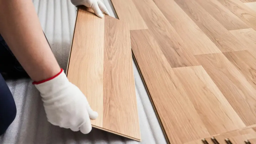 an installer wearing white gloves carefully locking a light hardwood flooring plank into place over a foam underlayment