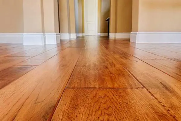 low-angle perspective of a polished, gleaming hardwood floor hallway with white baseboards, highlighting the results of proper hardwood flooring maintenance.