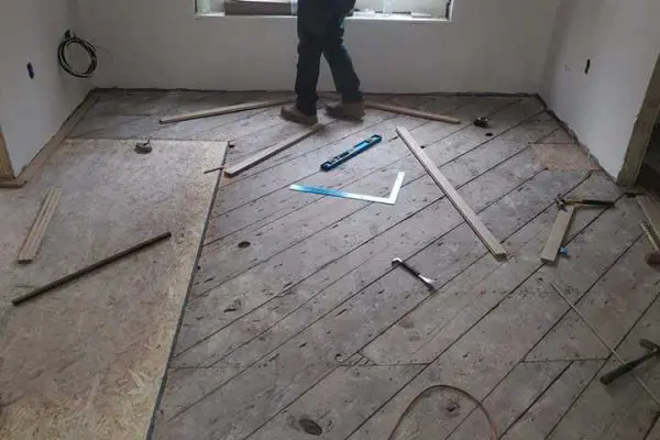 worker preparing a diagonal wood subfloor with leveling tools and measuring squares during a hardwood flooring replacement project
