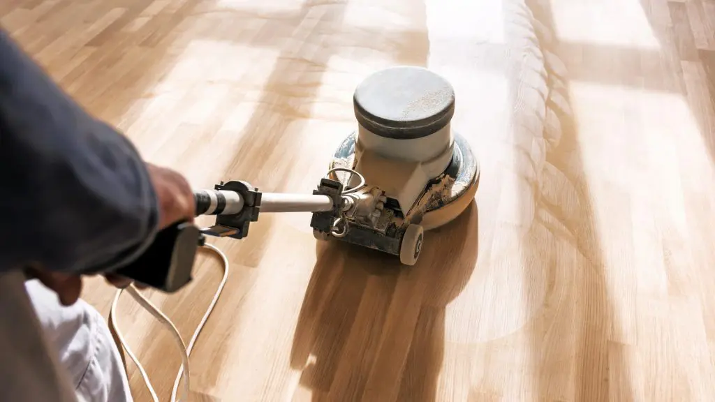 professional flooring contractor operating a heavy-duty buffer machine to sand and refinish a light hardwood floor