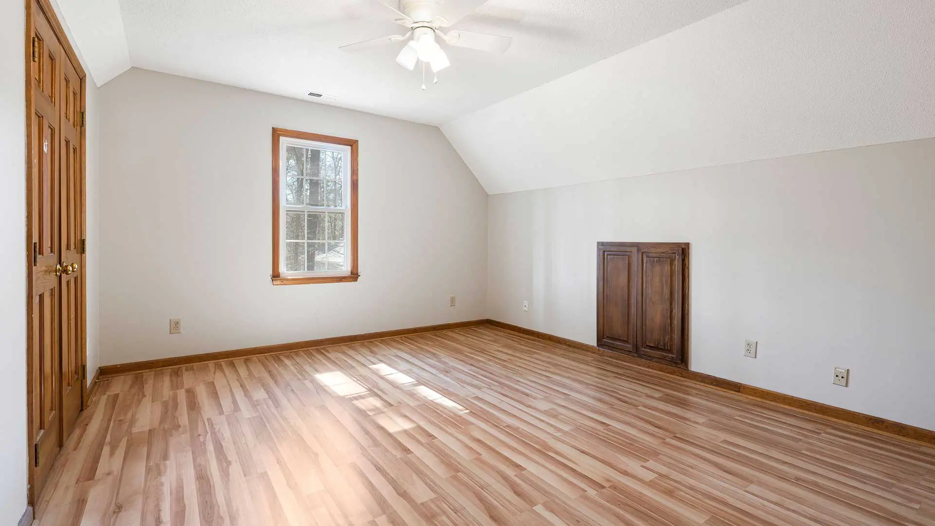 empty attic bedroom with sloped ceilings and light wood laminate flooring