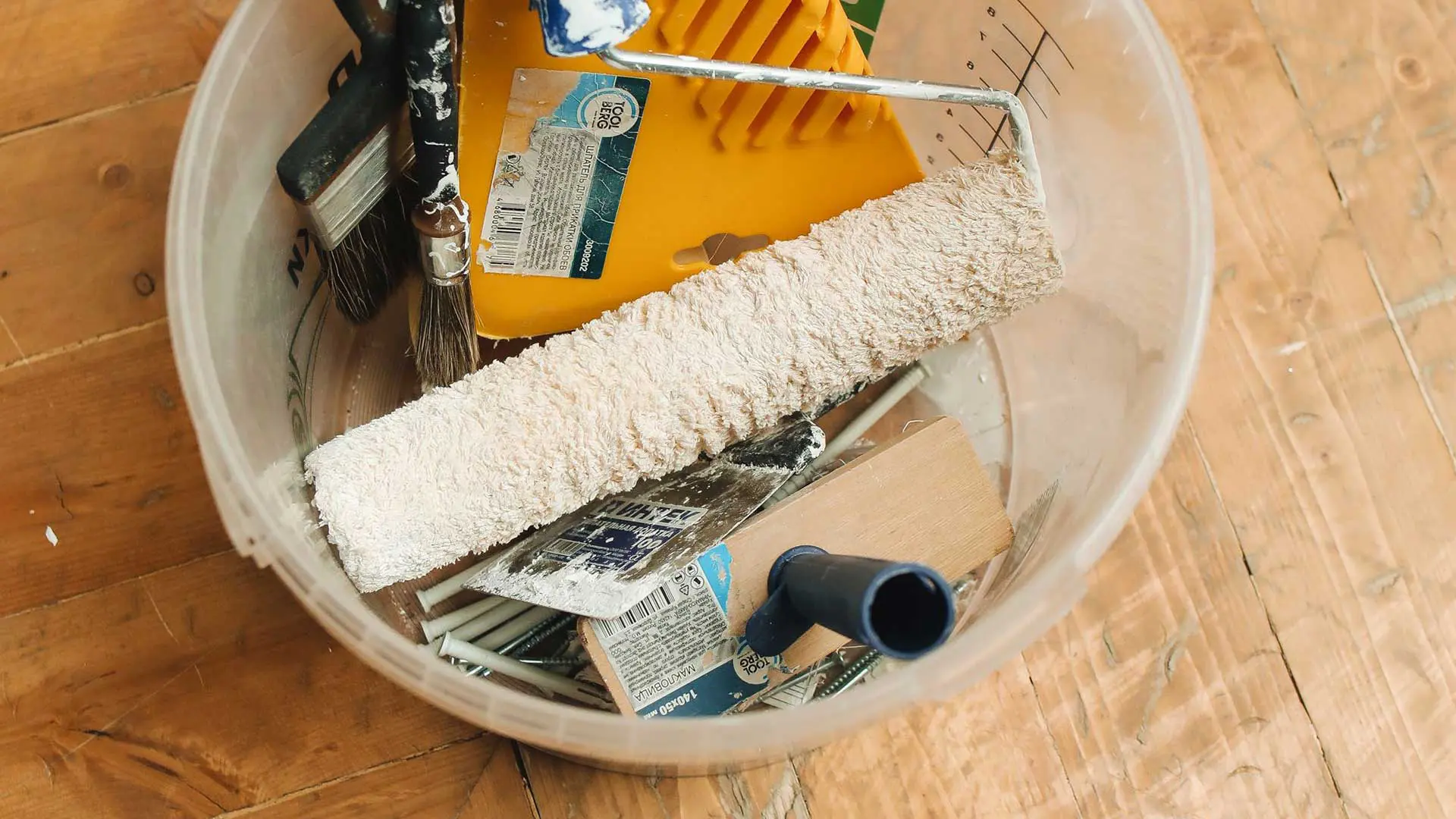 overhead view of a bucket containing a paint roller, brushes, and trowel