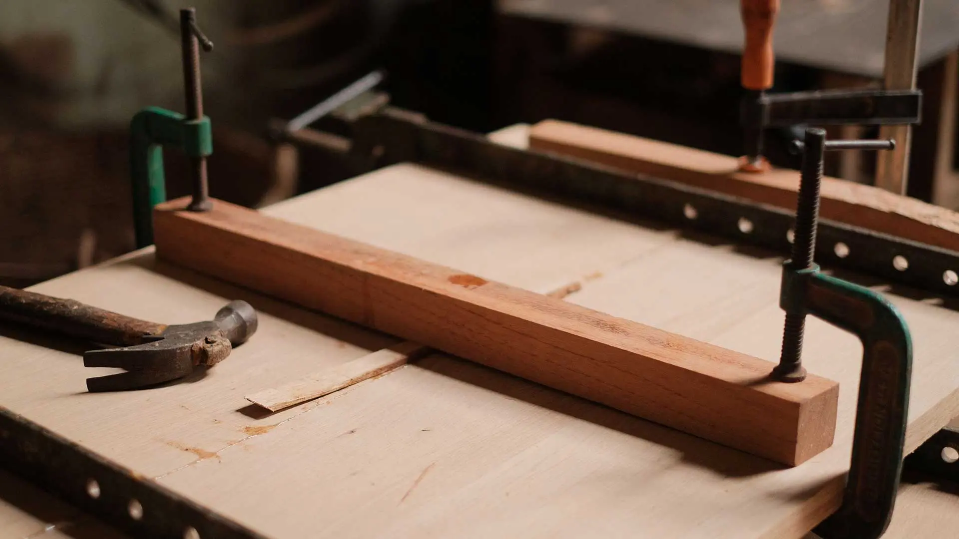 wooden boards clamped together next to an old hammer on a workbench.