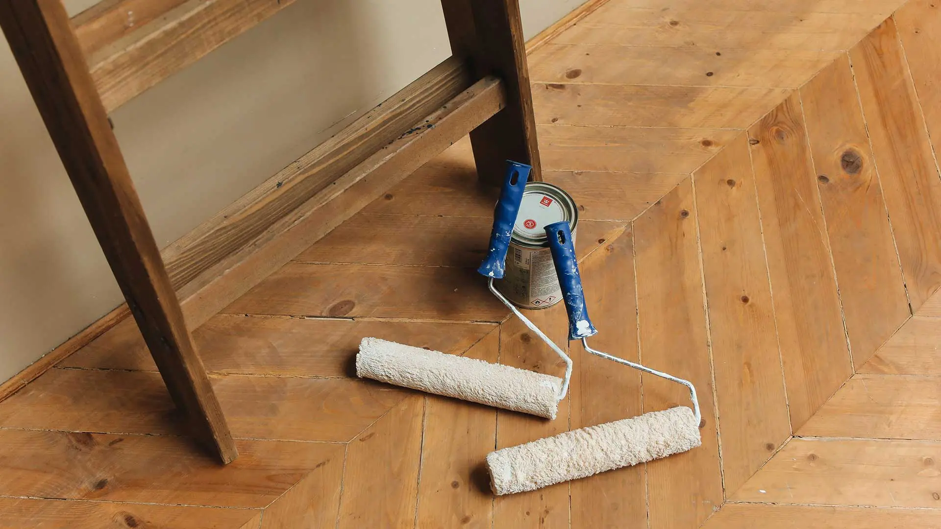 two paint rollers and a paint can on wooden herringbone flooring