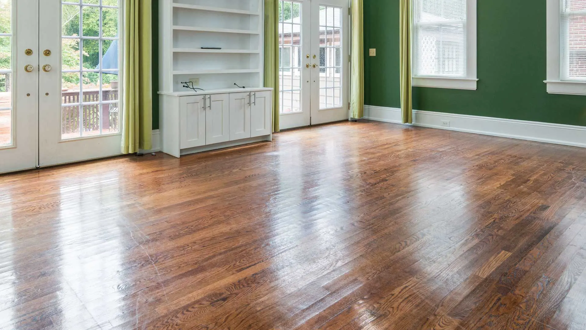 sunlit room featuring vibrant forest green walls, white built-in shelving, glass patio doors, and glossy, medium-dark hardwood floors