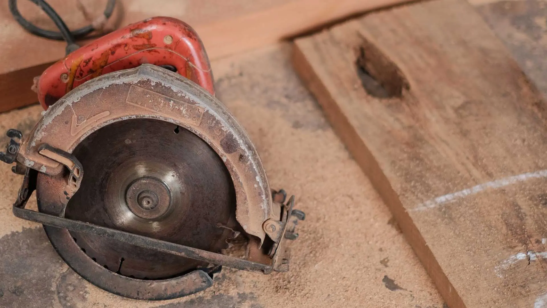 close-up view of a worn, rusty red circular power saw resting on a dusty workshop surface