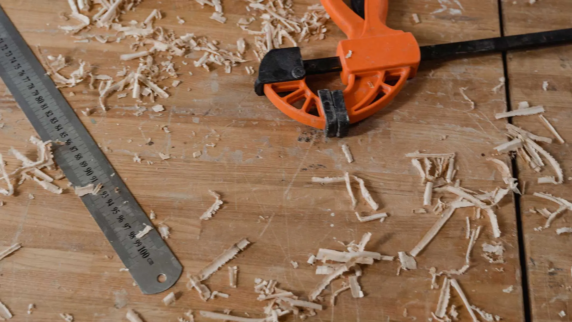 metal ruler, clamp, and wood shavings on a workbench surface.
