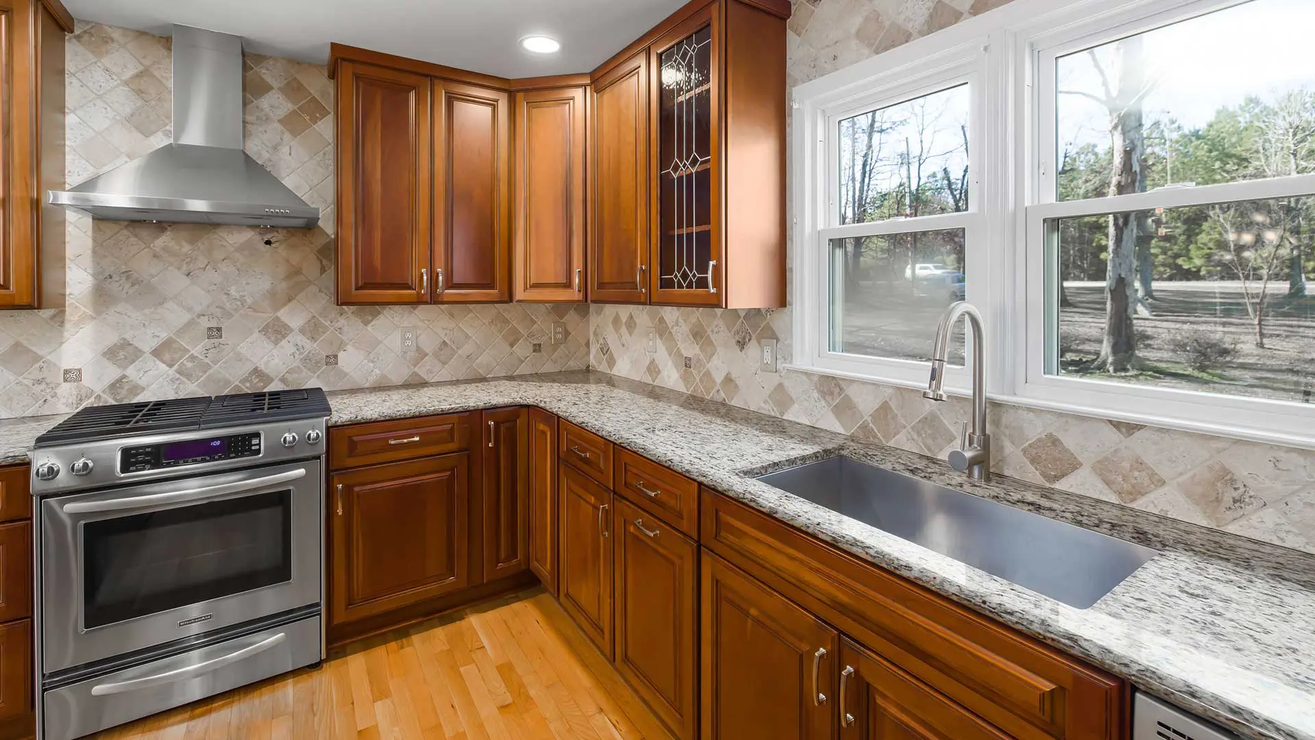 traditional kitchen corner showing warm wood cabinets, a large farmhouse sink with a gooseneck faucet under a window