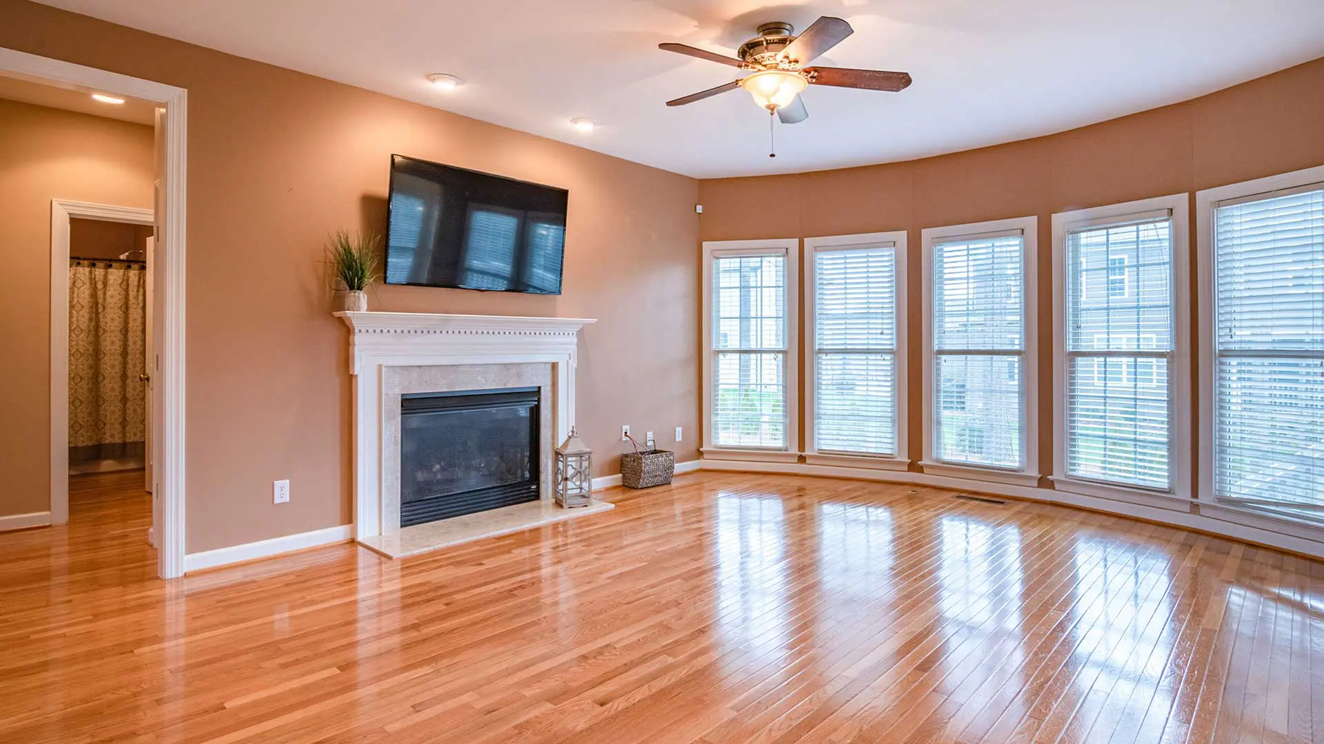 fireplace with a mantel, a ceiling fan, and high-gloss, polished hardwood-style flooring planks