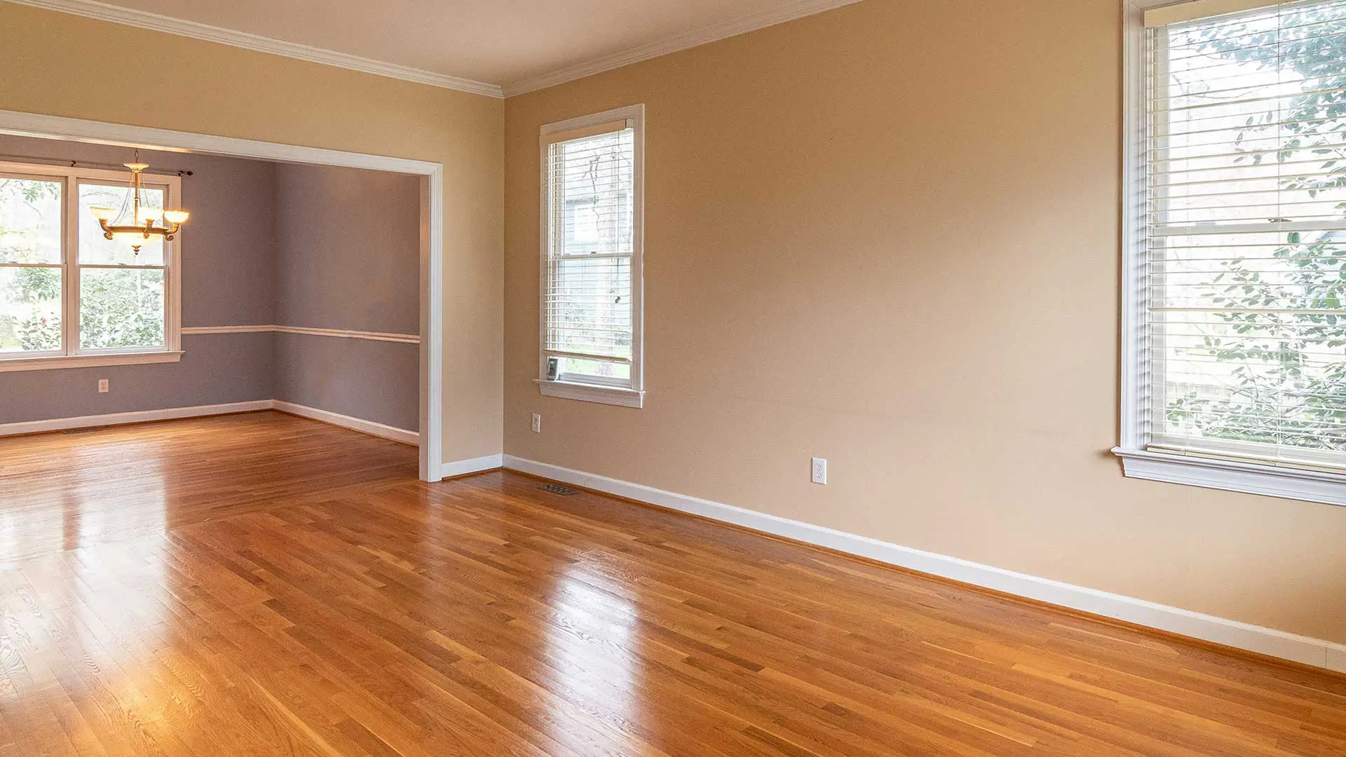 empty living room with beige walls and polished orange-brown hardwood floors