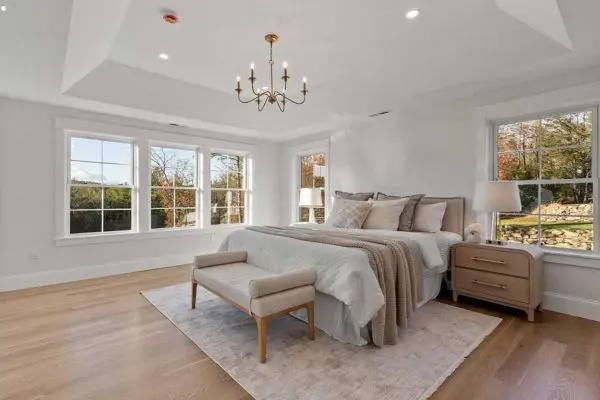 luxurious primary bedroom featuring beautifully installed light oak hardwood flooring and a recessed tray ceiling in revere ma