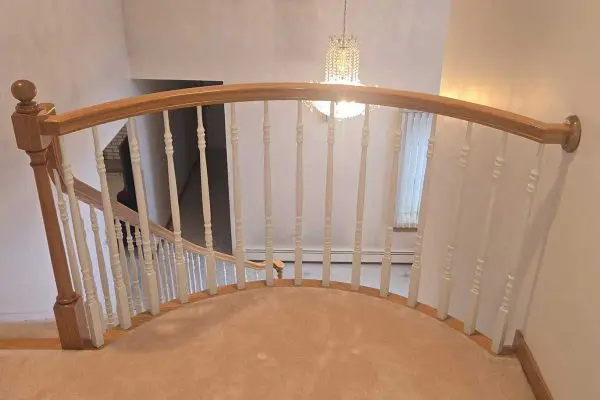 curved upper staircase landing with carpeted flooring overlooking a large hanging crystal chandelier in a revere ma home