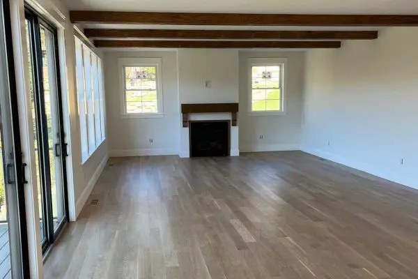 spacious living room featuring newly refinished light wood floors a fireplace and rustic ceiling beams in revere ma