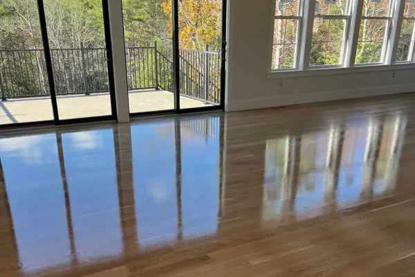 highly reflective gloss finish on newly installed hardwood flooring in a bright revere ma room with sliding glass doors