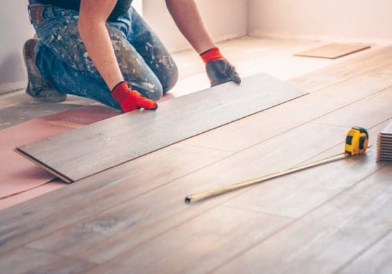 Contractor installing hardwood floor planks over underlayment during a carpet to hardwood conversion project