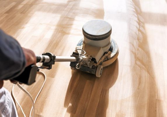 professional flooring contractor operating a heavy-duty buffer machine to sand and refinish a light hardwood floor